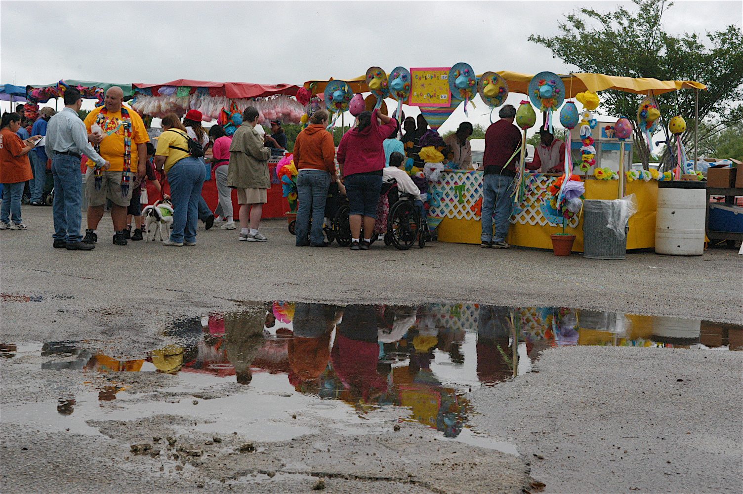 Group of people in line at a vendor at a small festival with a puddle in the foreground